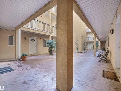 Courtyard common area featuring stamped concrete flooring, stucco walls, and covered walkways with white panel ceilings - #207 10606 102 Av Nw, Edmonton, AB 