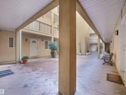 Courtyard common area featuring stamped concrete flooring, stucco walls, and covered walkways with white panel ceilings - 