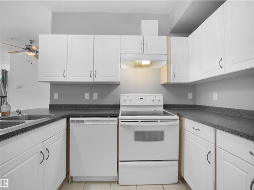 Kitchen featuring white cabinetry, dark speckled countertops, and a full suite of white appliances - #207 10606 102 Av Nw, Edmonton, AB 