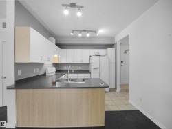 Kitchen featuring white cabinetry, dark countertops, a breakfast bar with wood-finish paneling, stainless steel sink, and track lighting - 