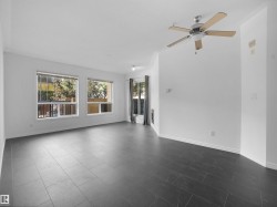 Spacious living area featuring large windows, dark tile flooring, white baseboards, a ceiling fan with light, and a built-in electric fireplace - 