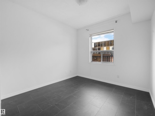 Bright interior space featuring a window with natural light, dark tile flooring, white walls, and white baseboards - #207 10606 102 Av Nw, Edmonton, AB 