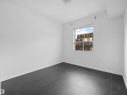 Bright interior space featuring a window with natural light, dark tile flooring, white walls, and white baseboards - 