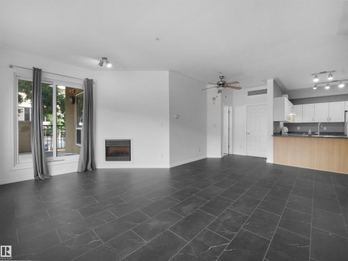Spacious open-concept living area featuring dark slate-style tile flooring, an electric fireplace, and a sliding glass door leading to an exterior balcony - #207 10606 102 Av Nw, Edmonton, AB 