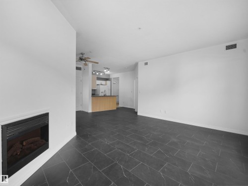 Open-concept living area featuring a built-in fireplace, dark tile flooring, and a ceiling fan - #207 10606 102 Av Nw, Edmonton, AB 