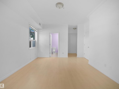 Spacious room featuring light wood-finish flooring, white baseboards, and bright white walls - #207 10606 102 Av Nw, Edmonton, AB 
