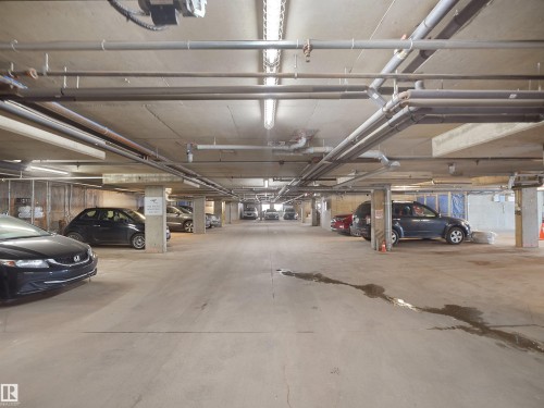Concrete underground parking garage with fluorescent lighting and overhead pipework - #207 10606 102 Av Nw, Edmonton, AB 