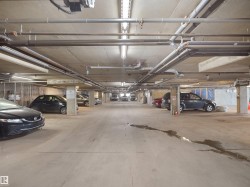 Concrete underground parking garage with fluorescent lighting and overhead pipework - 