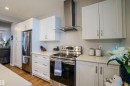 Modern kitchen featuring white cabinetry, stainless steel appliances, a stainless steel range hood, light-toned countertops, and wood-finish flooring - 1766 Dumont Crescent Sw, Edmonton, AB 