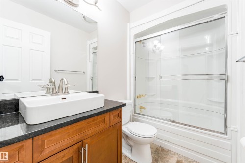 Bathroom featuring a rectangular vessel sink, dark countertop, wood-finish vanity, and a shower-tub combination with sliding glass doors - 5212 142 Street Nw, Edmonton, AB - Indoor Photo Showing Bathroom