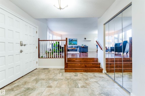 Entry foyer featuring large format tile flooring, a paneled entry door, a mirrored closet, and wood stairs with a white spindle railing - 5212 142 Street Nw, Edmonton, AB - Indoor Photo Showing Other Room