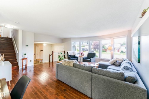 Spacious living area featuring expansive bay windows, wood-finish flooring, and a prominent staircase with wood treads and white risers - 5212 142 Street Nw, Edmonton, AB - Indoor Photo Showing Living Room