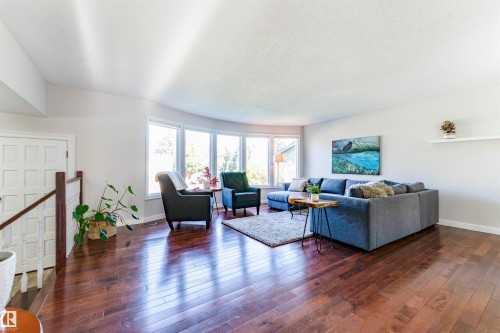 Spacious living area featuring polished wood-finish flooring, a curved wall of large windows, and white painted walls - 5212 142 Street Nw, Edmonton, AB - Indoor Photo Showing Living Room