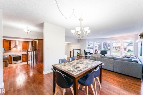 Open-concept interior featuring wood-finish flooring, a contemporary kitchen with stainless steel appliances, and a living area with a large bay window - 5212 142 Street Nw, Edmonton, AB - Indoor