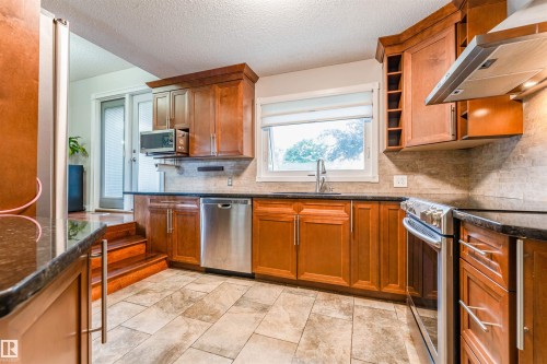 Spacious kitchen featuring warm wood cabinetry, dark countertops, a tile backsplash, and stainless steel appliances - 5212 142 Street Nw, Edmonton, AB - Indoor Photo Showing Kitchen