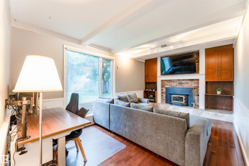 Living area with wood-finish flooring, a brick-surround fireplace, and built-in cabinetry - 5212 142 Street Nw, Edmonton, AB - Indoor Photo Showing Living Room With Fireplace