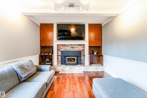 Living area featuring a brick fireplace with a wood-burning insert, integrated cabinetry, wood-finish flooring, and track lighting - 5212 142 Street Nw, Edmonton, AB - Indoor Photo Showing Living Room With Fireplace