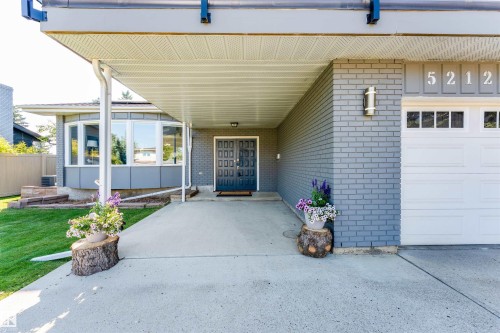 Covered entryway featuring a bay window, concrete driveway, attached garage with window inserts, and grey brick exterior - 5212 142 Street Nw, Edmonton, AB - Outdoor With Exterior