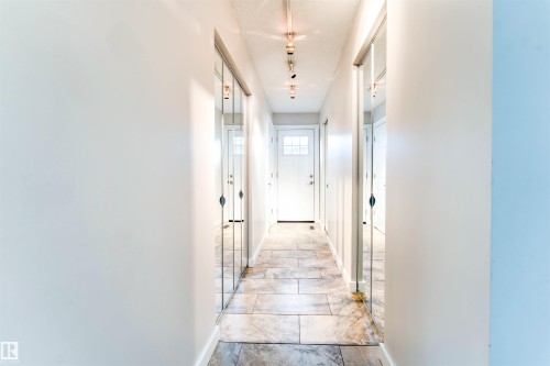 Hallway featuring rectangular tile flooring, mirrored closet doors, track lighting, and a white paneled door with window inserts - 5212 142 Street Nw, Edmonton, AB - Indoor Photo Showing Other Room