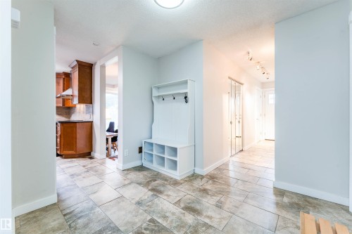 Spacious entryway featuring large format tile flooring, a built-in white storage bench with coat hooks, track lighting, and a mirrored closet - 5212 142 Street Nw, Edmonton, AB - Indoor Photo Showing Other Room