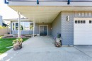 Covered entryway featuring a bay window, concrete driveway, attached garage with window inserts, and grey brick exterior - 5212 142 Street Nw, Edmonton, AB 