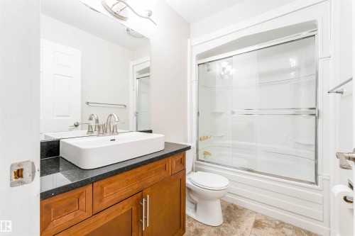 Contemporary bathroom featuring a dark wood-finish vanity with a vessel sink, a dark countertop, and a shower-tub combination with sliding glass doors - 5212 142 Street Nw, Edmonton, AB - Indoor Photo Showing Bathroom