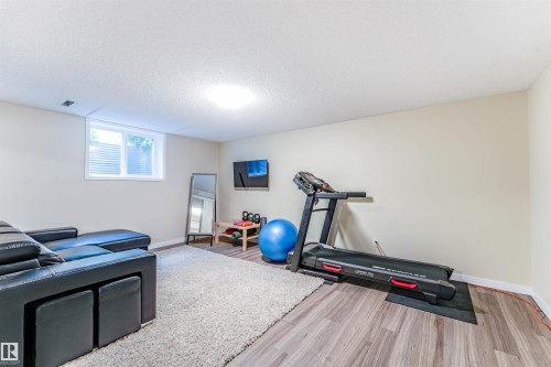 Versatile recreation room featuring wood-finish flooring, a neutral color palette, and a window for natural light - 5212 142 Street Nw, Edmonton, AB - Indoor Photo Showing Gym Room