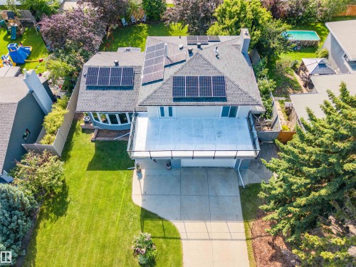 Exterior featuring a light-colored facade, dark shingle roof with multiple solar panel installations, a large elevated deck with dark railings, a concrete driveway, and a manicured front lawn - 5212 142 Street Nw, Edmonton, AB - Outdoor