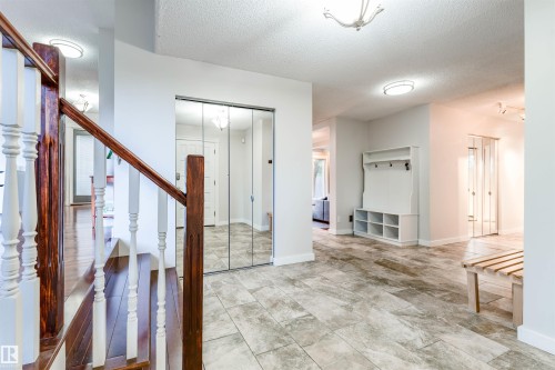 Entrance foyer featuring tile flooring, mirrored closet doors, a built-in coat rack with cubby storage, and a hardwood staircase with white balusters - 5212 142 Street Nw, Edmonton, AB - Indoor Photo Showing Other Room