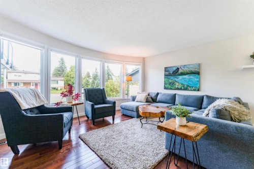 Living area featuring a curved wall of large windows, wood-finish flooring, light neutral-toned walls, and a recessed ceiling - 5212 142 Street Nw, Edmonton, AB - Indoor Photo Showing Living Room