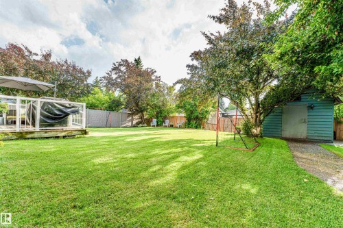 Expansive rear yard featuring a wooden deck with glass railing, detached shed, mature trees, and privacy fencing - 5212 142 Street Nw, Edmonton, AB - Outdoor