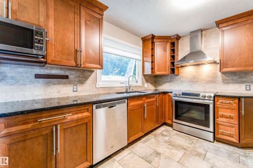 Kitchen featuring wood cabinetry, stainless steel appliances, granite countertops, and a tiled backsplash - 5212 142 Street Nw, Edmonton, AB - Indoor Photo Showing Kitchen