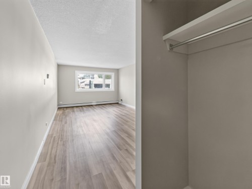 Open room featuring wood-finish flooring, a large window, light-toned walls, and a built-in closet with shelving and a hanging rod - #502 9710 105 St Nw, Edmonton, AB 