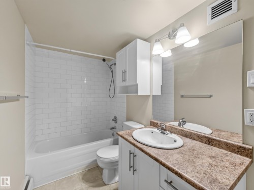 Full bathroom featuring a shower-over-tub with subway tile surround, a white vanity with a laminate countertop, and a mirrored wall - #502 9710 105 St Nw, Edmonton, AB 