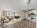 Open-concept living area featuring wood-finish flooring, white kitchen cabinetry, and large window - #502 9710 105 St Nw, Edmonton, AB 
