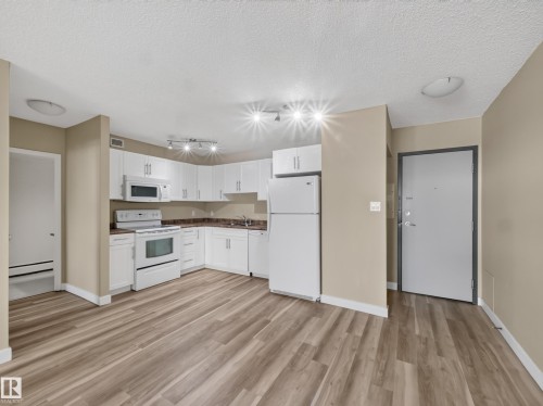 Open-concept kitchen featuring white cabinetry, a complete suite of white appliances, track lighting, and wood-finish flooring - #502 9710 105 St Nw, Edmonton, AB 