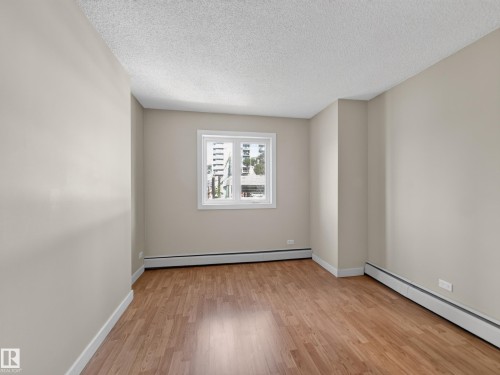 Room with light neutral wall paint, wood-finish flooring, white baseboards, and a white-framed window - #502 9710 105 St Nw, Edmonton, AB 
