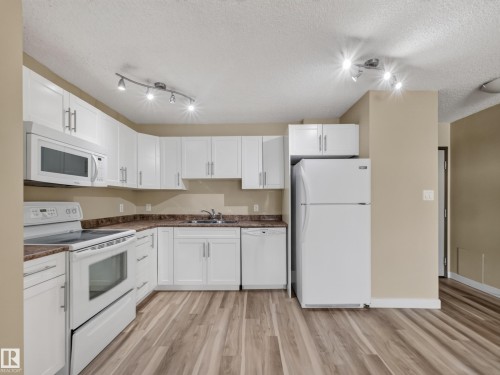 Kitchen featuring white cabinetry, white appliances, wood-finish flooring, and track lighting - #502 9710 105 St Nw, Edmonton, AB 