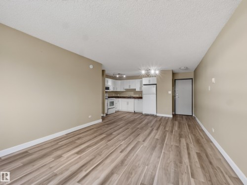 Open-concept living space featuring wood-finish flooring, neutral wall paint, and white trim - #502 9710 105 St Nw, Edmonton, AB 
