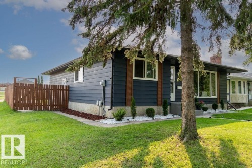 Exterior featuring dark blue horizontal siding, white trim windows, brown privacy fence, manicured lawn, and white rock landscaping - 27 Apache Crescent, Leduc, AB 