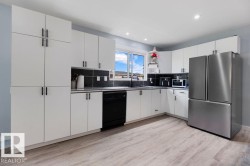 Modern kitchen featuring white cabinetry, black hardware, black stone countertops, and wood-finish flooring - 