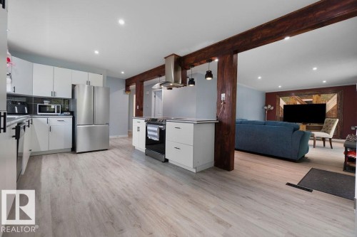 Modern kitchen featuring stainless steel appliances, white cabinetry with dark hardware, and light wood-finish flooring throughout - 27 Apache Crescent, Leduc, AB 