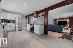 Modern kitchen featuring stainless steel appliances, white cabinetry with dark hardware, and light wood-finish flooring throughout - 