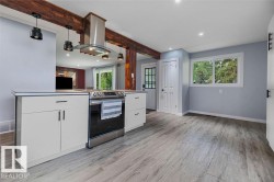 Kitchen featuring exposed wood beams, stainless steel range with overhead ventilation, light-toned wood-finish flooring, white cabinetry with dark hardware, and recessed lighting - 