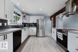 Kitchen featuring white cabinetry with black hardware, wood-finish flooring, a stainless steel refrigerator, and dark stone-look backsplash - 