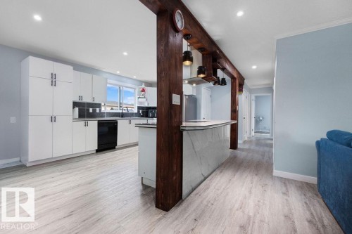 Open-concept kitchen featuring white cabinetry with dark pulls, dark backsplash tiling, and dark appliances - 27 Apache Crescent, Leduc, AB 