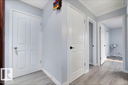 Hallway featuring light gray walls, white trim, wood-finish flooring, and multiple white panel doors with contrasting hardware - 