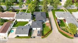 Residential property featuring a detached garage with a dark shingle roof, a paved driveway, and a fenced backyard with mature trees - 