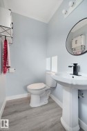 Pedestal sink with a matte black faucet, wall-mounted mirror, wood-finish flooring, and crown molding - 