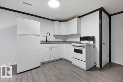 Kitchen featuring white cabinetry, gray countertop, black gooseneck faucet, white refrigerator, and white electric range - 